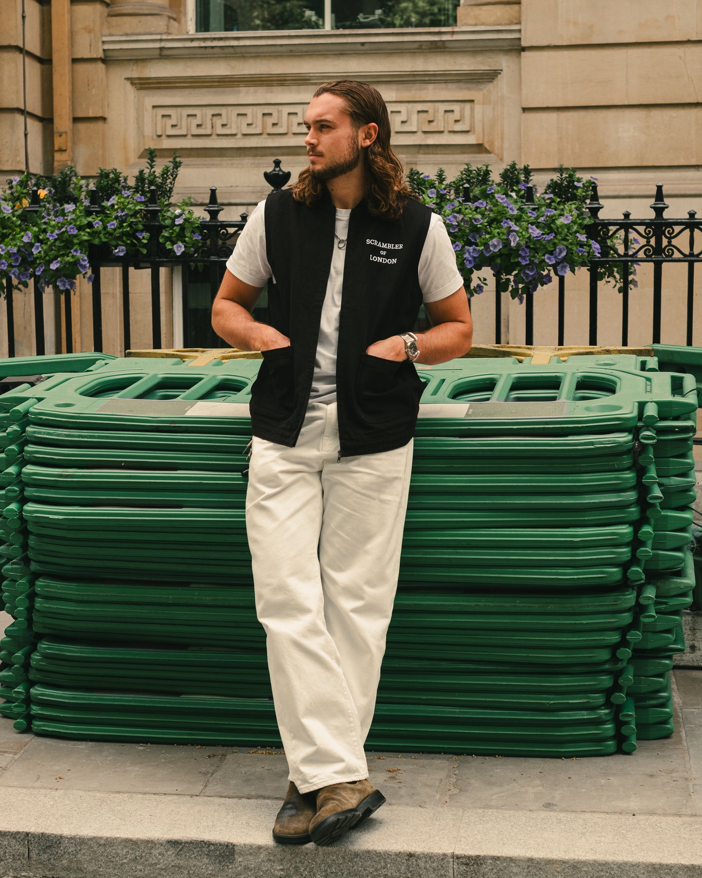 Man wearing The Canvas Vest by Scrambler of London, leaning on a wall with sunglasses and a London townhouse behind.