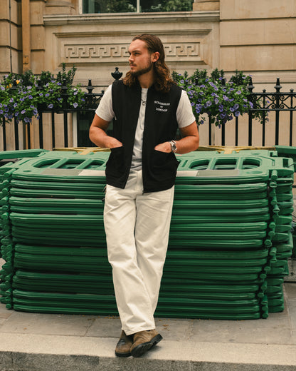 Man wearing The Canvas Vest by Scrambler of London, leaning on a wall with sunglasses and a London townhouse behind.